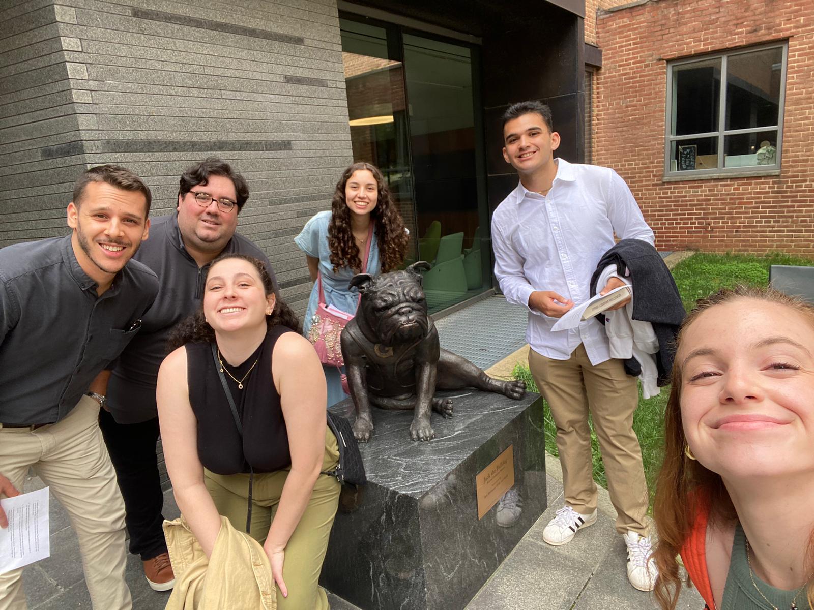 A group of six people posing for a selfie with a statue of Jack the Bulldog outside of the Healy Student Center at Georgetown University.