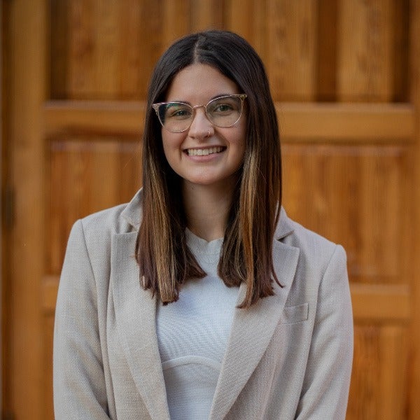 Samantha Kelley wearing a light-colored suit, standing in front of a wall.