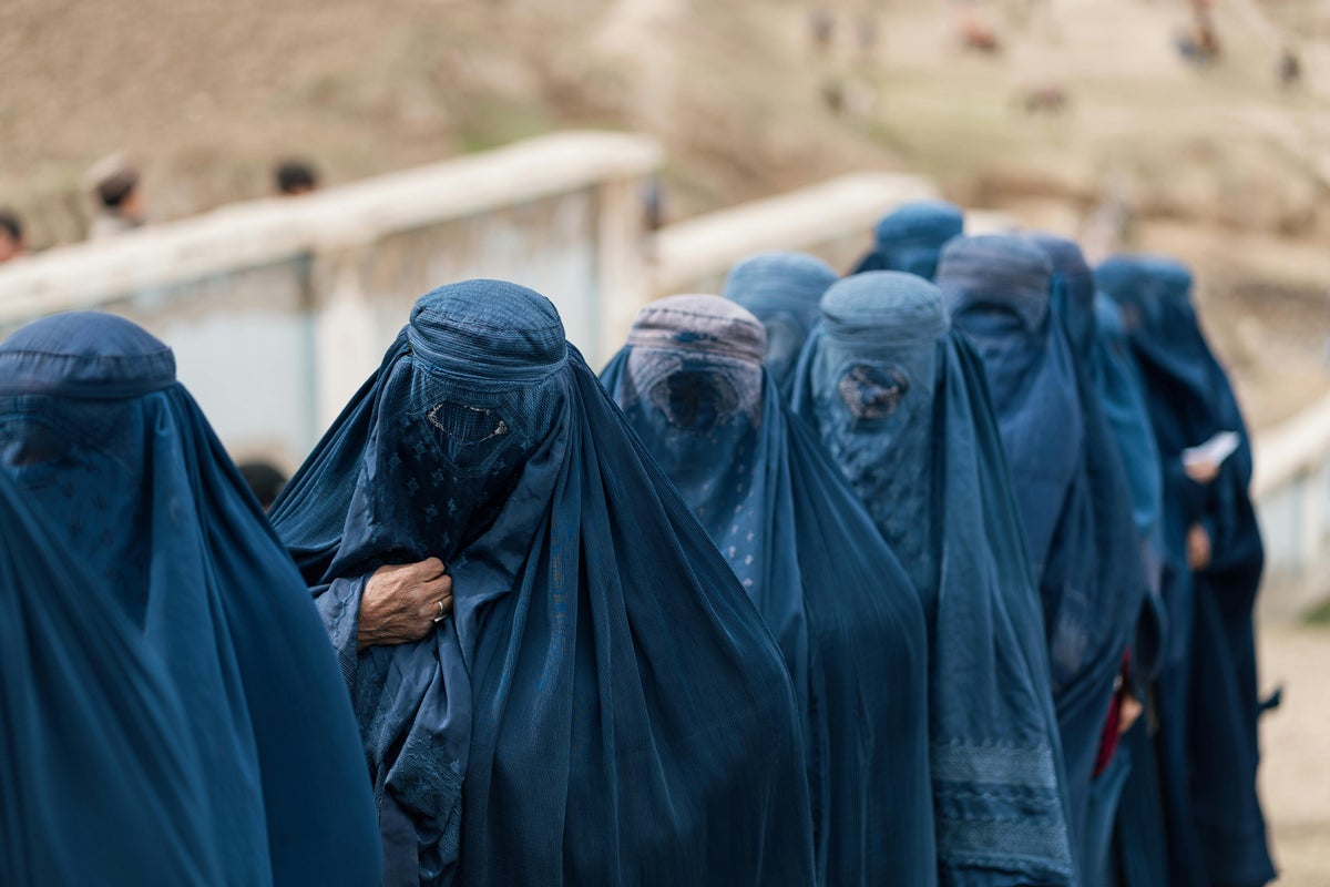 A group of individuals wearing full-length blue burqas stand or walk in a line outdoors.
