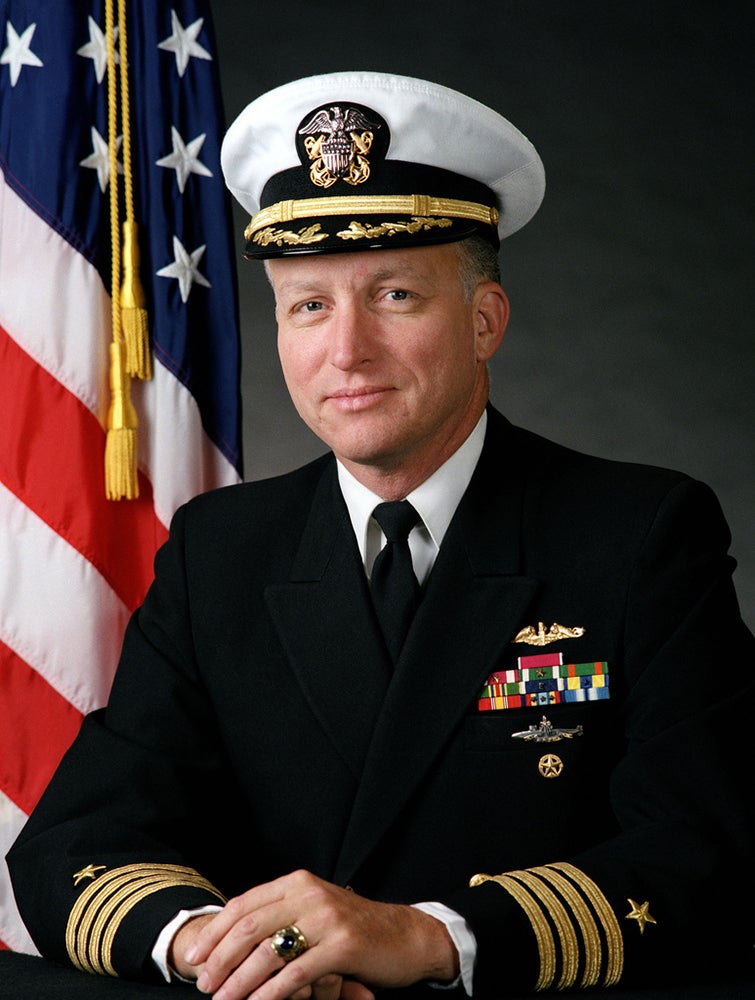 Official military portrait of U.S. Navy Captain Hugh M. Doherty (SSP'93)  in a dark dress uniform with medals and an American flag background.