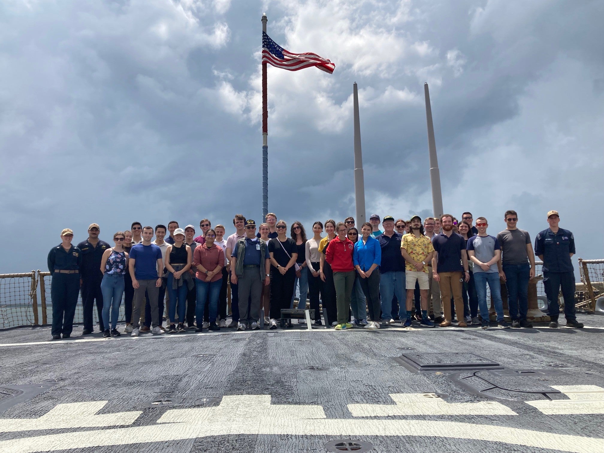 A large group of students standing in front of a US flag on a cloudy day
