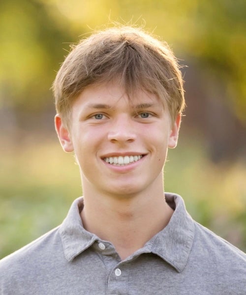 A person with short blonde hair wearing a gray polo shirt.