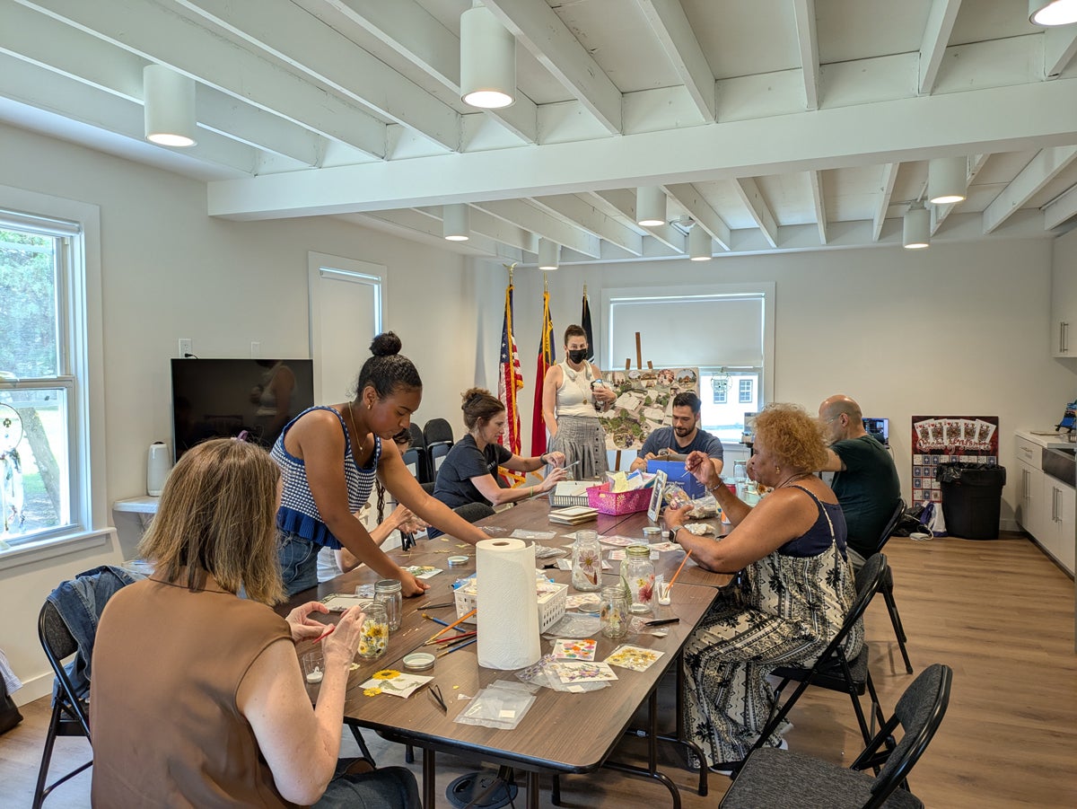 A group of people seated around a table in a well-lit room, engaging in various arts and crafts activities.