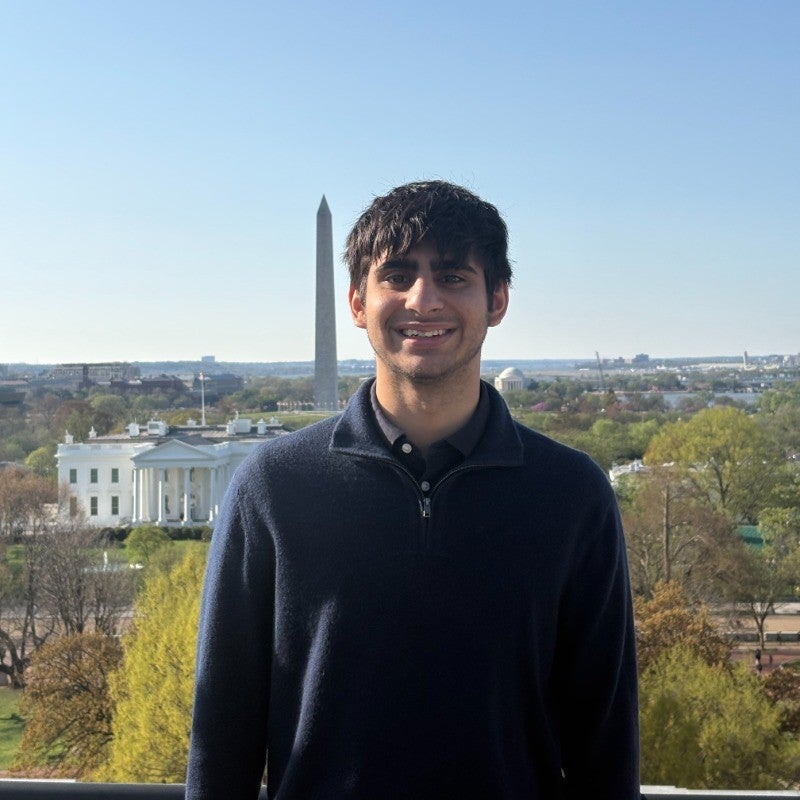 An individual wearing a black shirt posing with the Washington monument visible in the background.