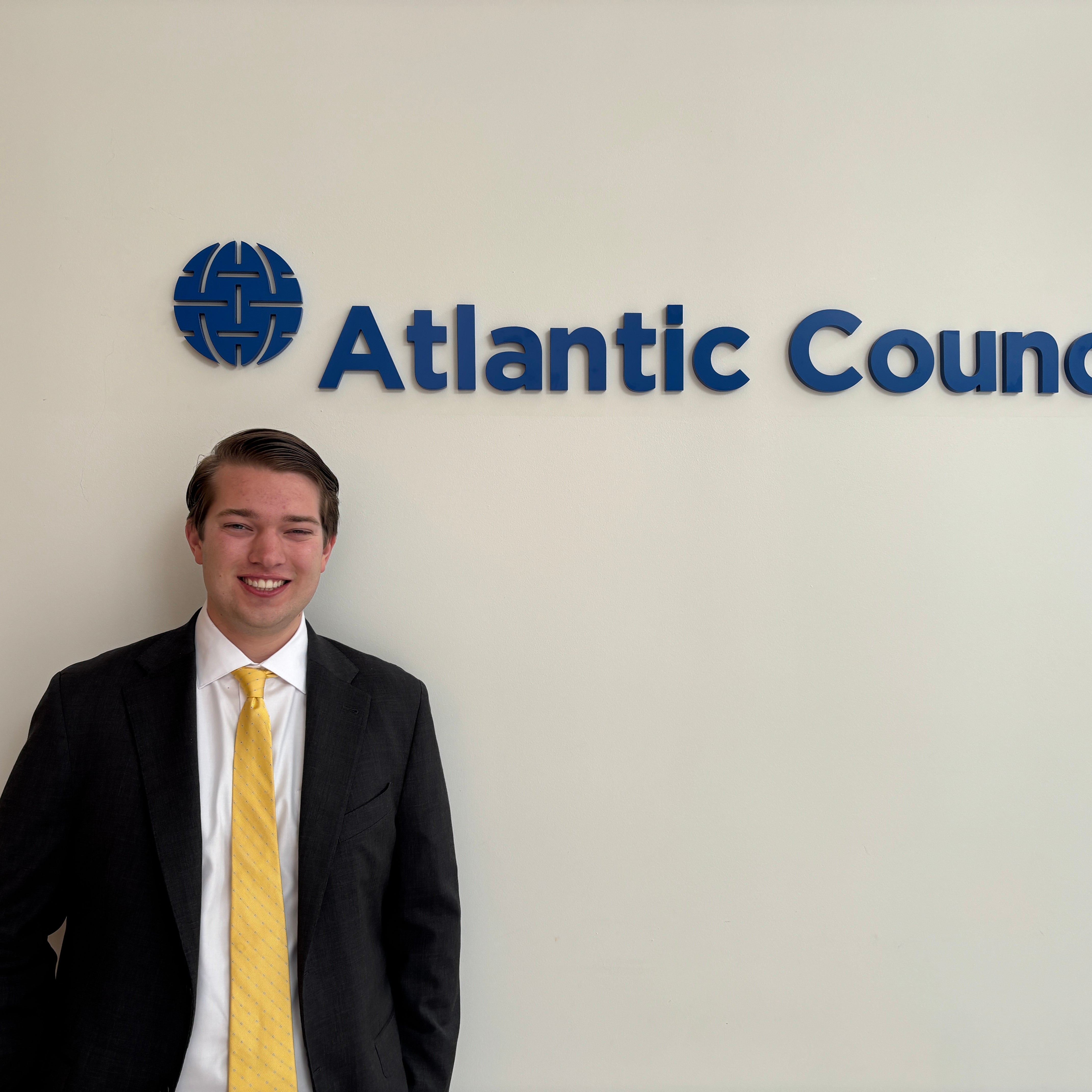A person in formal attire stands next to a wall with the Atlantic Council logo.
