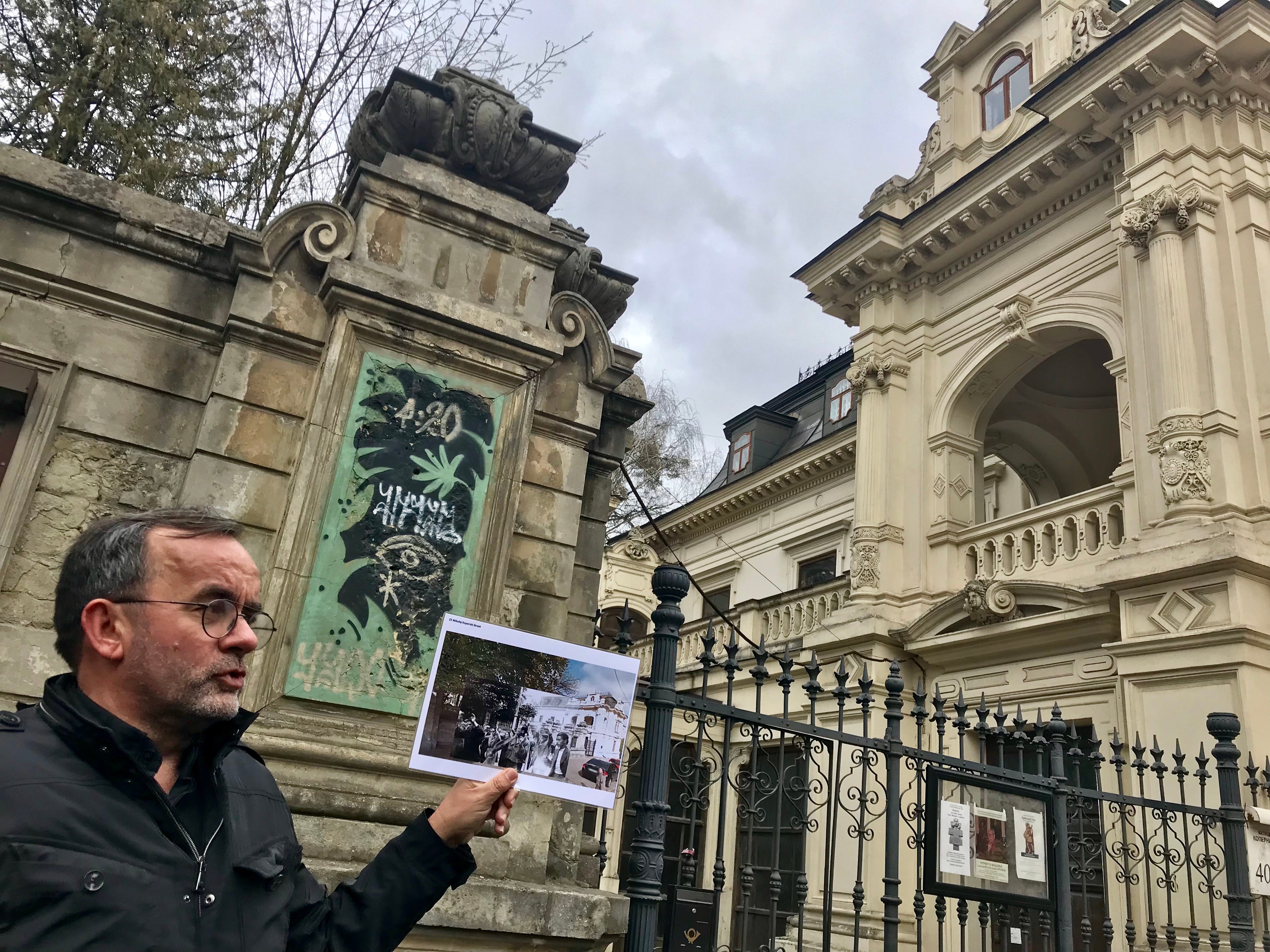 A man holds up a photo in front of a building.