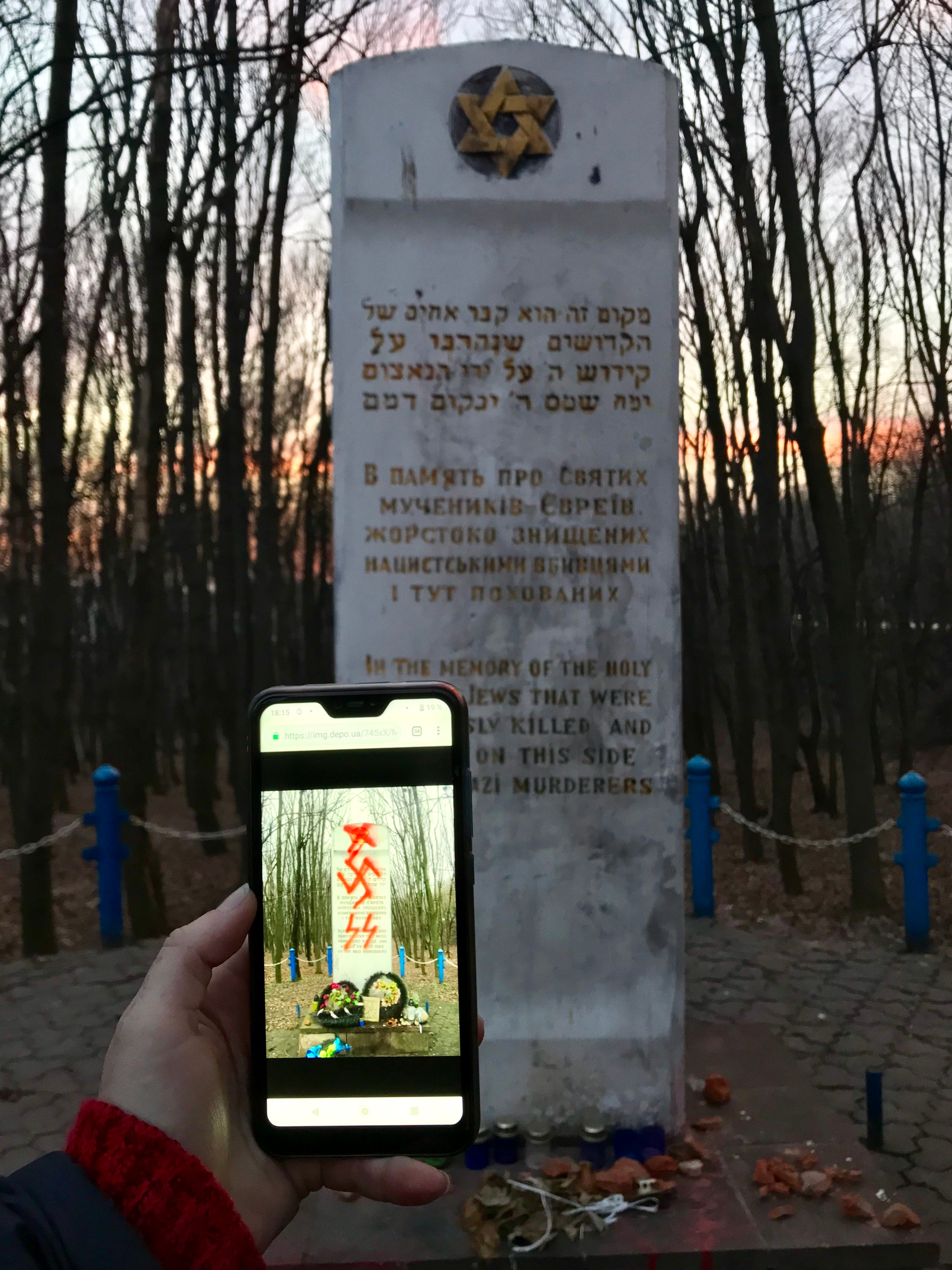 A phone showing graffiti on a memorial in the foreground while the cleaned memorial is in the background.